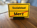 Ortsausgangsschild „Sozialstaat / Merz“ mit Standfuß - Subthiel - Marco Thiel